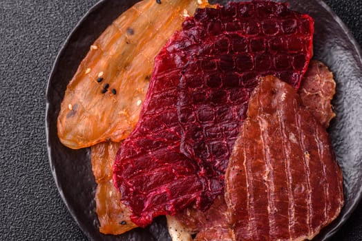 Jerky, dried meat in the form of slices with salt, spices and herbs on a dark concrete background