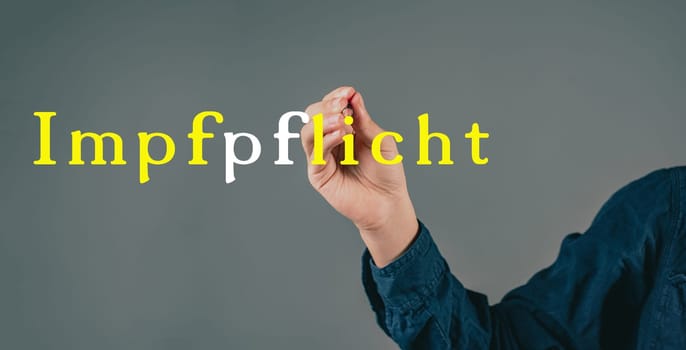Mandatory vaccination is standing in german language on a grey background, hand with a pen is writing the message