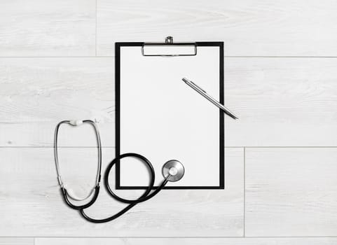 Photo of blank medical clipboard, stethoscope and pen on wooden background. Copy space. Flat lay.