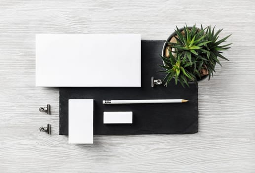 Corporate identity template. Blank envelope, business card, pencil, eraser, clips and succulent plant on stone board. Flat lay.