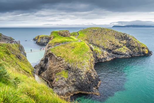 People on the Carrick a Rede rope bridge and scenic island surrounded by turquoise Atlantic Ocean, Wild Atlantic Way, Northern Ireland