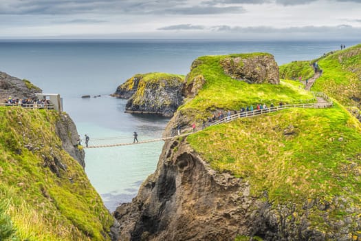 People queueing to crossing Carrick a Rede rope bridge to access island surrounded by turquoise Atlantic Ocean, Wild Atlantic Way, Northern Ireland