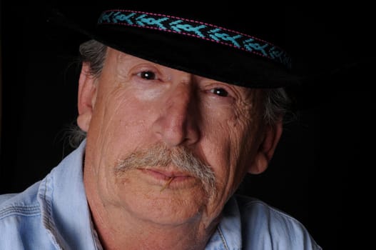 Portrait of an old senior cowboy with hat isolated over black