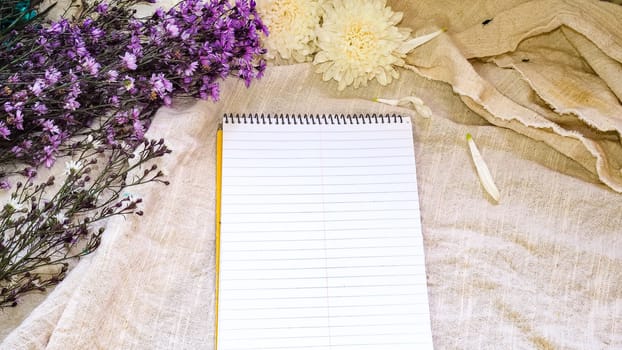 Blank paper and flower decoration. Greeting card on a white natural  linen background. Top view. Copy space.