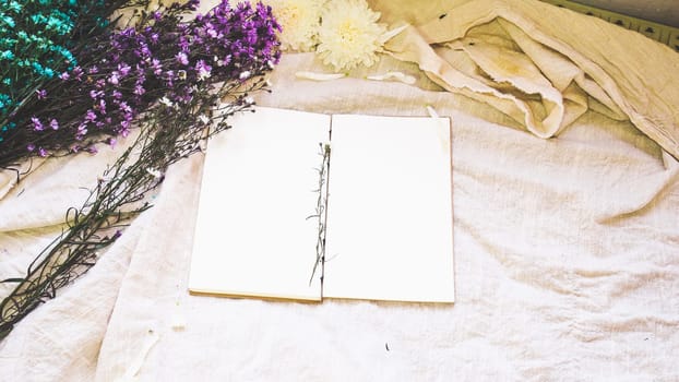 Blank white paper notebook and flower decoration. Greeting card on a white natural  linen background. Top view. Copy space.