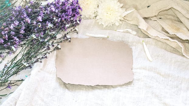 Blank craft paper and flower decoration. Greeting card on a white natural  linen background. Top view. Copy space.