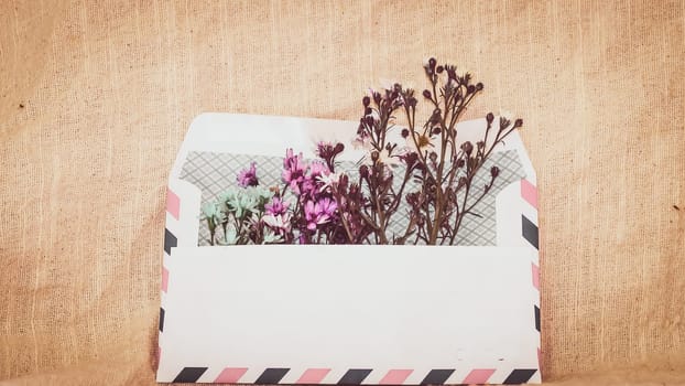 Opened envelope with small little flowers arrangements on linen background, top view. Festive greeting concept.