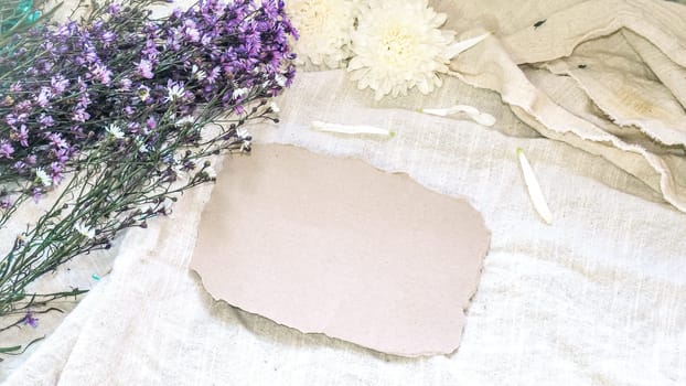 Blank craft paper and flower decoration. Greeting card on a white natural  linen background. Top view. Copy space.