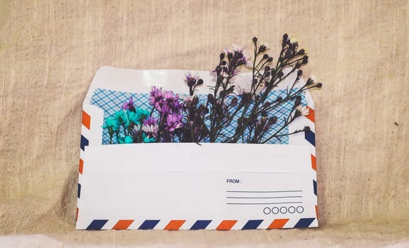 Opened envelope with small little flowers arrangements on linen background, top view. Festive greeting concept.