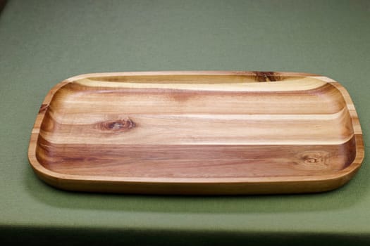 Acacia hard wood rectangle serve tray shown horizontally wide on a green table cloth background close up. Empty rectangular wooden tray made of hard wood acacia on a green tablecloth background..