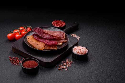 Jerky, dried meat in the form of slices with salt, spices and herbs on a dark concrete background