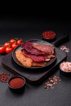 Jerky, dried meat in the form of slices with salt, spices and herbs on a dark concrete background