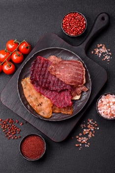 Jerky, dried meat in the form of slices with salt, spices and herbs on a dark concrete background