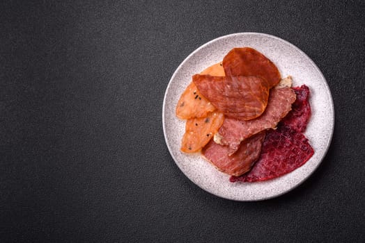 Jerky, dried meat in the form of slices with salt, spices and herbs on a dark concrete background