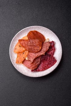 Jerky, dried meat in the form of slices with salt, spices and herbs on a dark concrete background