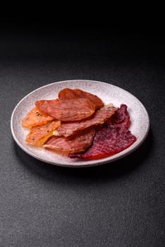 Jerky, dried meat in the form of slices with salt, spices and herbs on a dark concrete background