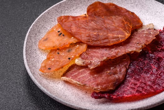 Jerky, dried meat in the form of slices with salt, spices and herbs on a dark concrete background
