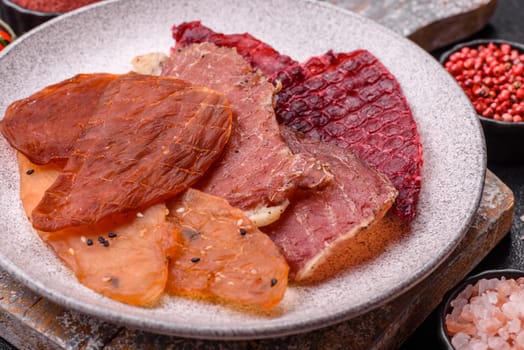 Jerky, dried meat in the form of slices with salt, spices and herbs on a dark concrete background