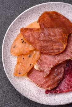 Jerky, dried meat in the form of slices with salt, spices and herbs on a dark concrete background
