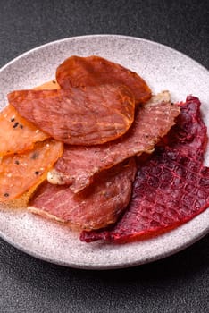 Jerky, dried meat in the form of slices with salt, spices and herbs on a dark concrete background