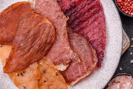 Jerky, dried meat in the form of slices with salt, spices and herbs on a dark concrete background