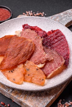 Jerky, dried meat in the form of slices with salt, spices and herbs on a dark concrete background