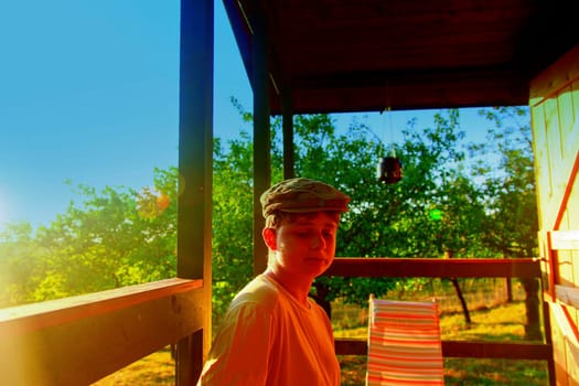 The young boy is sitting on a verandah. Dreamy and romantic image. Summer and happy childhood concept. Added sun flare effect.