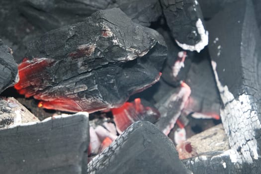 Fire on logs in fire pot with embers and burning coal. Bonfire with blazing red and orange fire flames. Fire background with woods and planks on fire at night view.