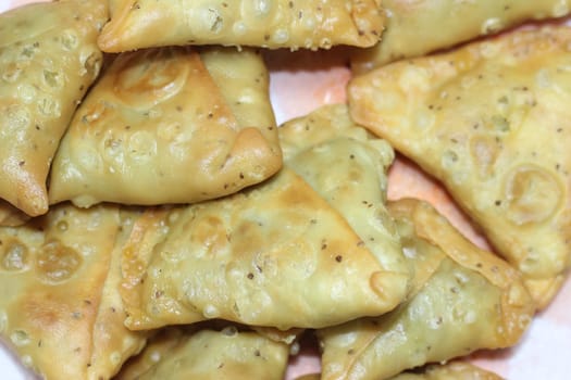 Closeup of delicious home made spicy and crunchy samosa pastries placed in a white ceramic plate on wooden floor