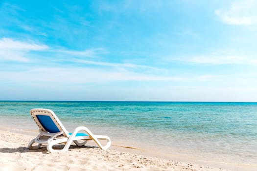 A lone white blue sun lounger stands on the seashore right next to the water. The concept of a beach holiday by the sea or ocean. Private beach of the hotel. Quiet calm sea side. High quality photo
