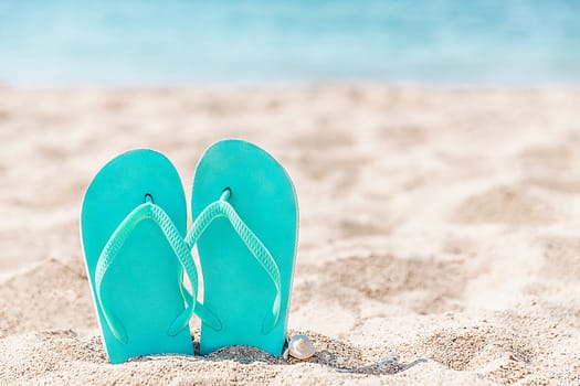 Turquoise or light blue flip flops or sandal shoe stuck in the sand on sandy beach by the sea coastline or ocean. Travel or vacation concept in hot countries in summer or winter. High quality photo