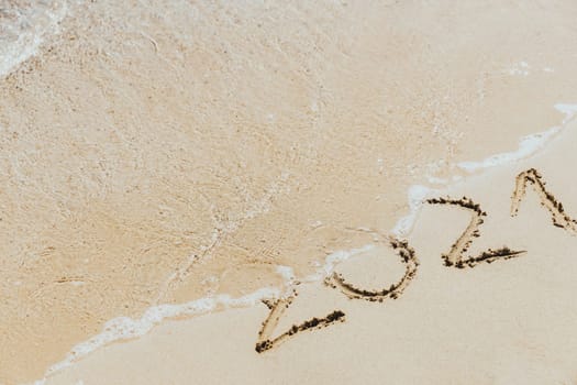 Waves wash away the inscription on the sand 2021. Concept of the outgoing year 2021. Celebrating the new year on the seashore. Holidays for the Christmas holidays. High quality photo