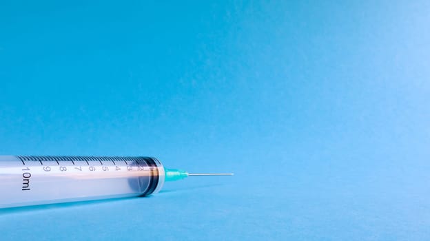 On a blue background lies a medical syringe with a needle. epidemic. Copy space The concept of collecting blood and injection vaccines, medical equipment for hypodermic injection, healthcare theme