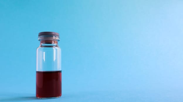 One glass transparent bottle with red medicine for vaccines on a blue background on a medical theme with copy space. Medical vaccination against the concept of coronavirus flu