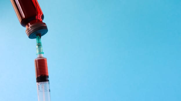 Coronavirus flu and pandemic vaccines, syringe and vial with red liquid on a blue background. medical concept, subcutaneous injection, treatment of the disease. Copy space for text or logo.