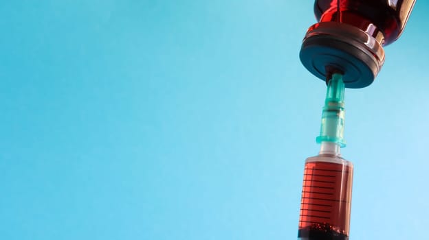 A syringe sticks out of a red liquid bottle. Isolated on a blue background. Medicine, injections, vaccines and disposable syringes, drug concept. Sterile bottle. Glass ampoule medical for injection
