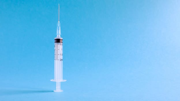 On a blue background lies a medical syringe with a needle. epidemic. Copy space The concept of collecting blood and injection vaccines, medical equipment for hypodermic injection, healthcare theme