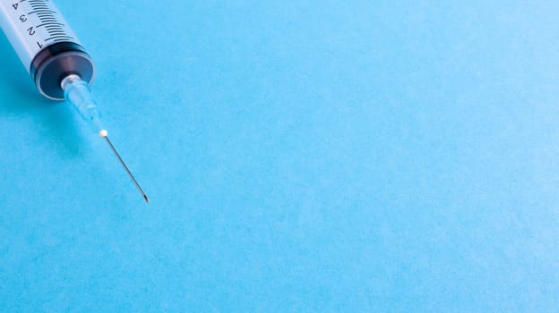 On a blue background lies a medical syringe with a needle. epidemic. Copy space The concept of collecting blood and injection vaccines, medical equipment for hypodermic injection, healthcare theme