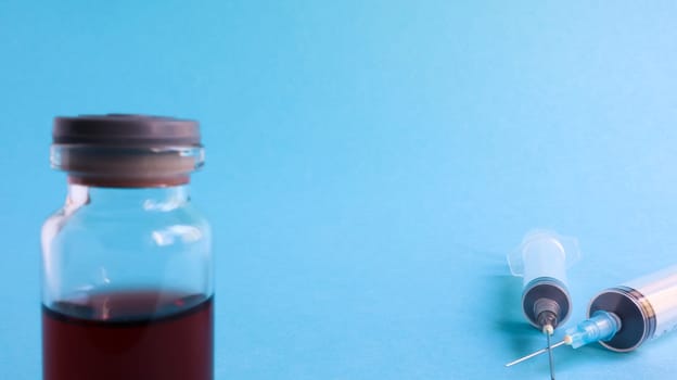 One medical glass bottle with red potion on a blue background and two medical disposable syringes with a needle. Medical concept shows a medical test tube and vaccines against coronavirus. Copy place.