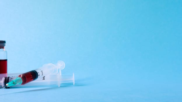 One medical glass bottle with red potion on a blue background and two medical disposable syringes with a needle. Medical concept shows a medical test tube and vaccines against coronavirus. Copy place.