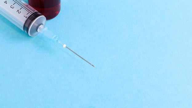 One medical glass bottle with red potion on a blue background and a medical disposable syringe with a needle. Medical concept shows a medical test tube and vaccines against coronavirus. Copy place.