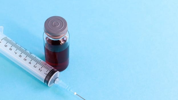 One medical glass bottle with red potion on a blue background and a medical disposable syringe with a needle. Medical concept shows a medical test tube and vaccines against coronavirus. Copy place.