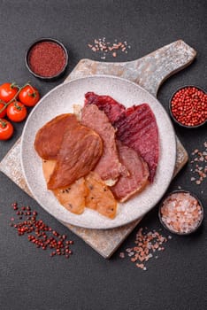 Jerky, dried meat in the form of slices with salt, spices and herbs on a dark concrete background