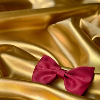 Red bow tie on draped golden satin