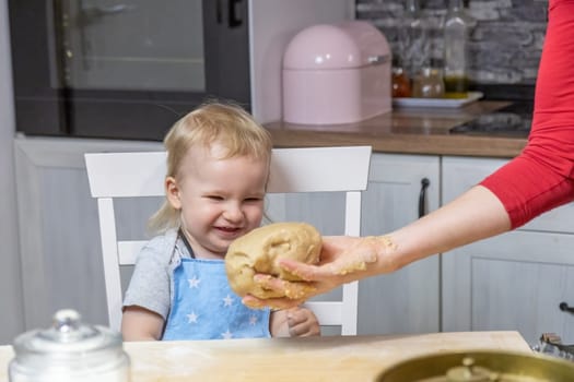 Adorable little child boy is laughing at the dough that a woman's hand is giving him. Horizontally.