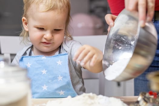 Blond little child boy is helpful in baking in domestic kitchen, indoors. Horizontally.