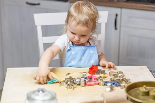 Adorable funny blond little child boy cuts out the dough in domestic kitchen. Horizontally.