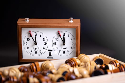 The Chess pieces on a board and a chess clock on a dark background