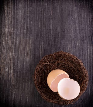 The broun broken egg shells in the nest on wooden surface