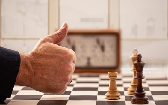 The hand and chessboard with figures and clock on blurred window background. Selective focus